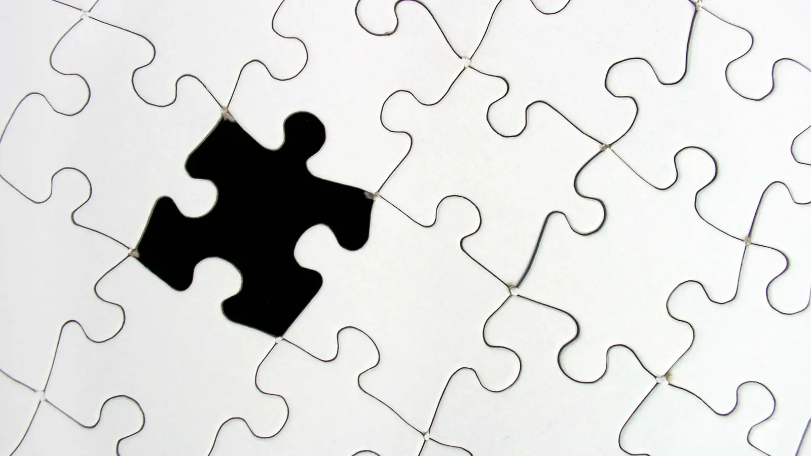 A white jigsaw puzzle with one black piece-shaped gap where a piece is missing.