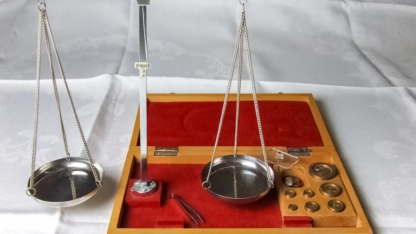 A jeweller balance scale with hanging pans, set in a wooden case with red felt and weights.