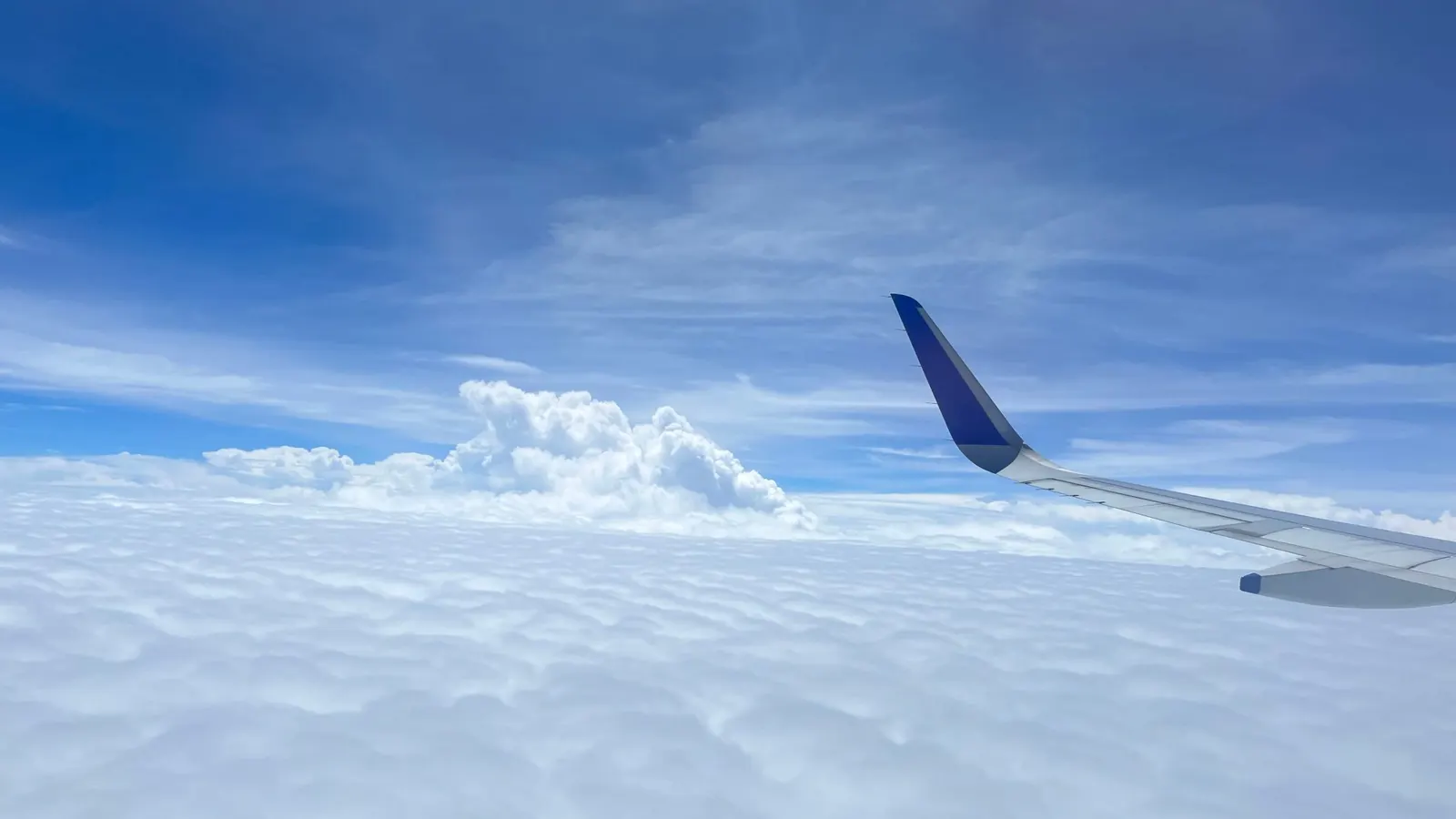 A jet's wing and winglet over a bright layer of white clouds under a clear blue sky