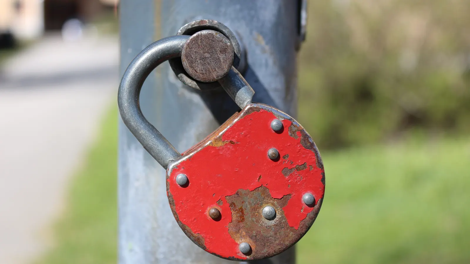 A red padlock hangs from a metal post against a blurred green background.