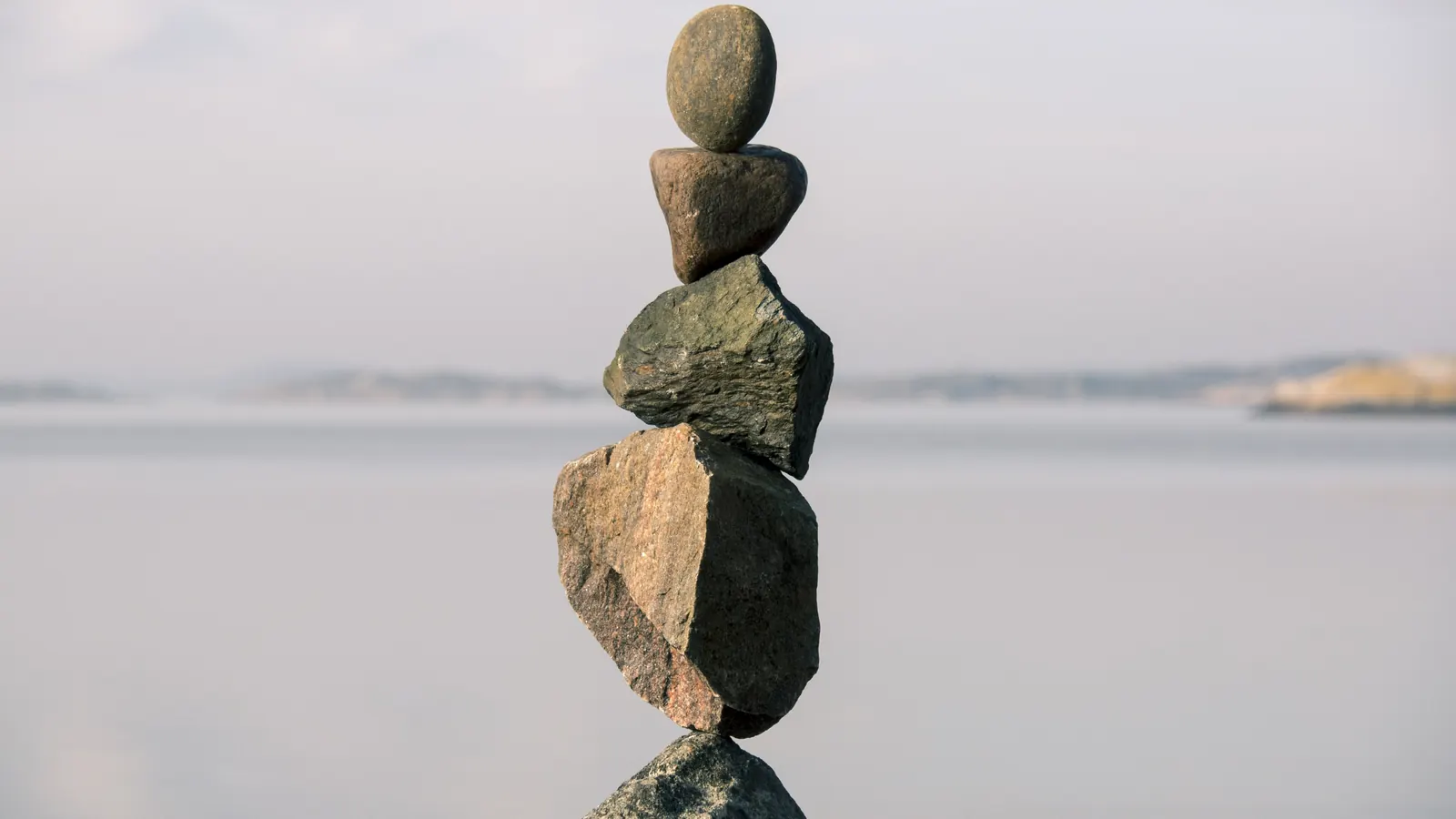 A tower of gray and brown stones balanced one on top of another above a calm gray lake