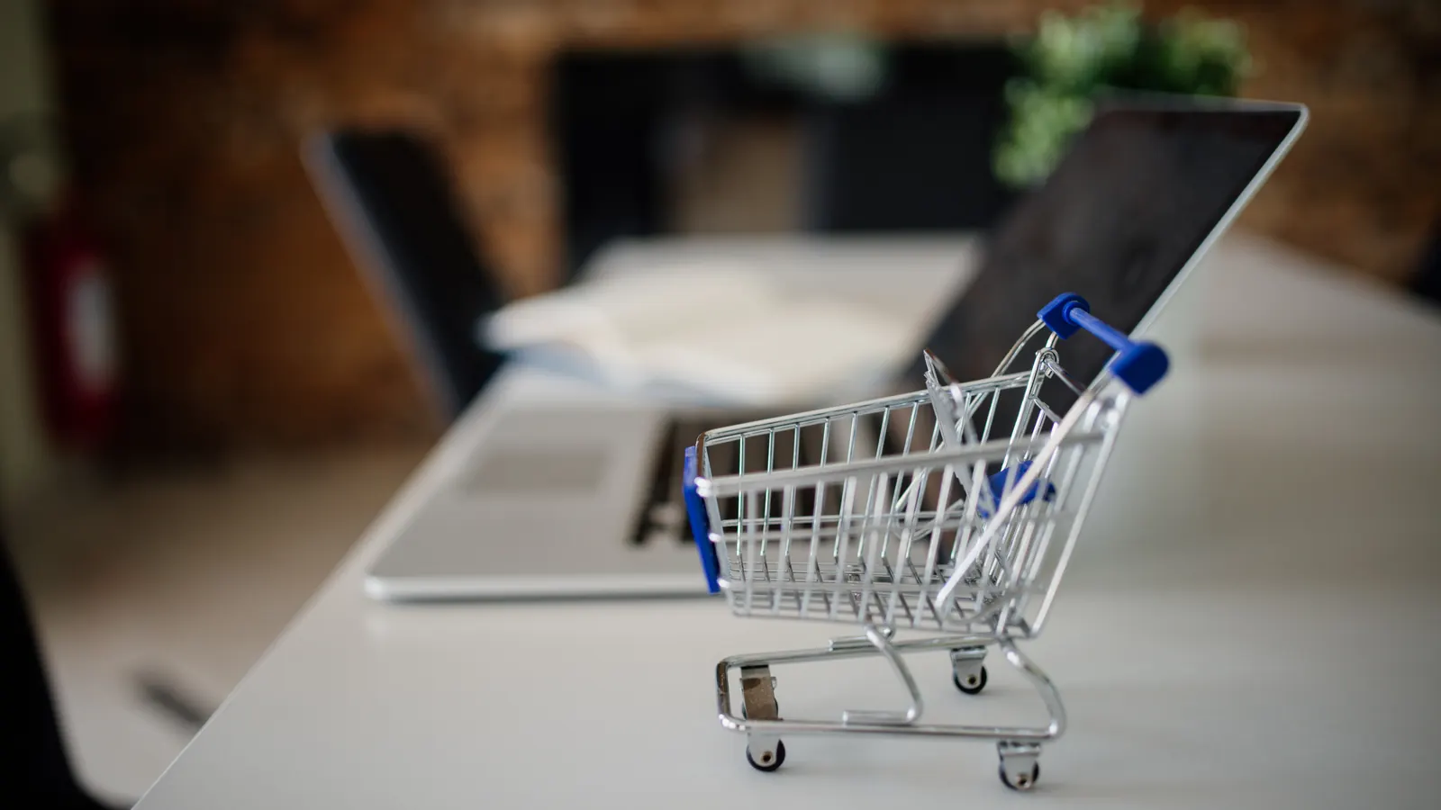 A small toy shopping cart sits on a table beside an open laptop.
