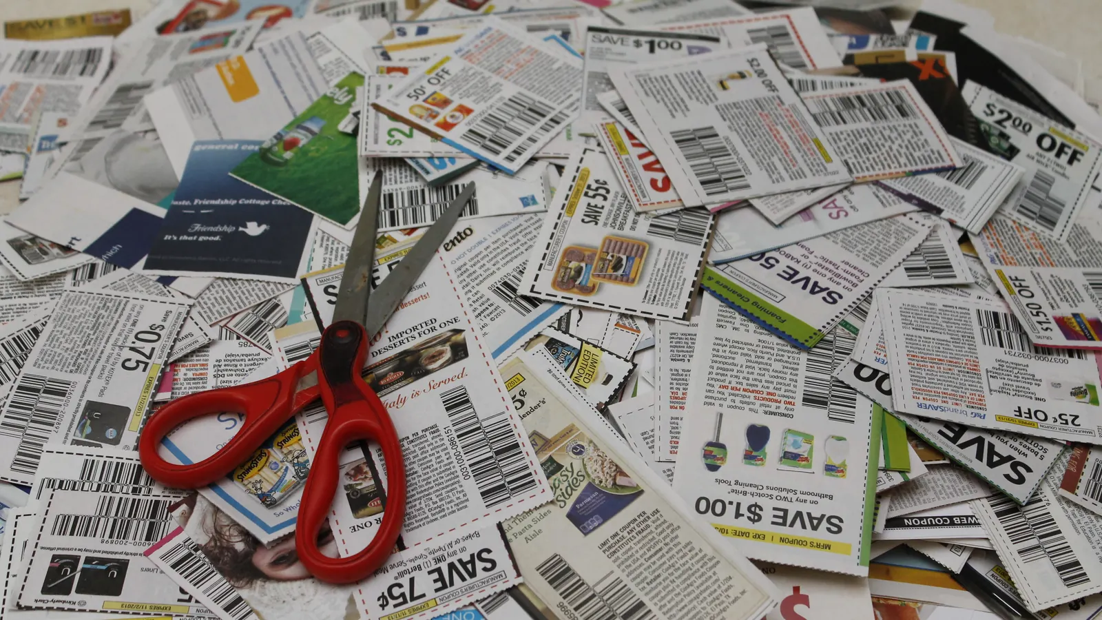 A pile of paper coupons with a pair of red-handled scissors resting on top.