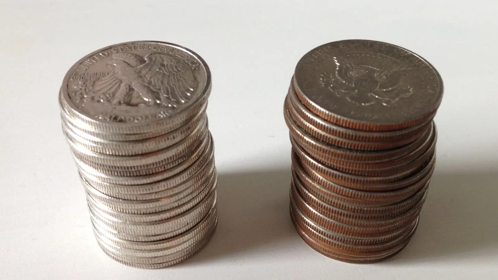 Two stacks of coins side by side on a white surface, one silver-toned and one copper-toned.