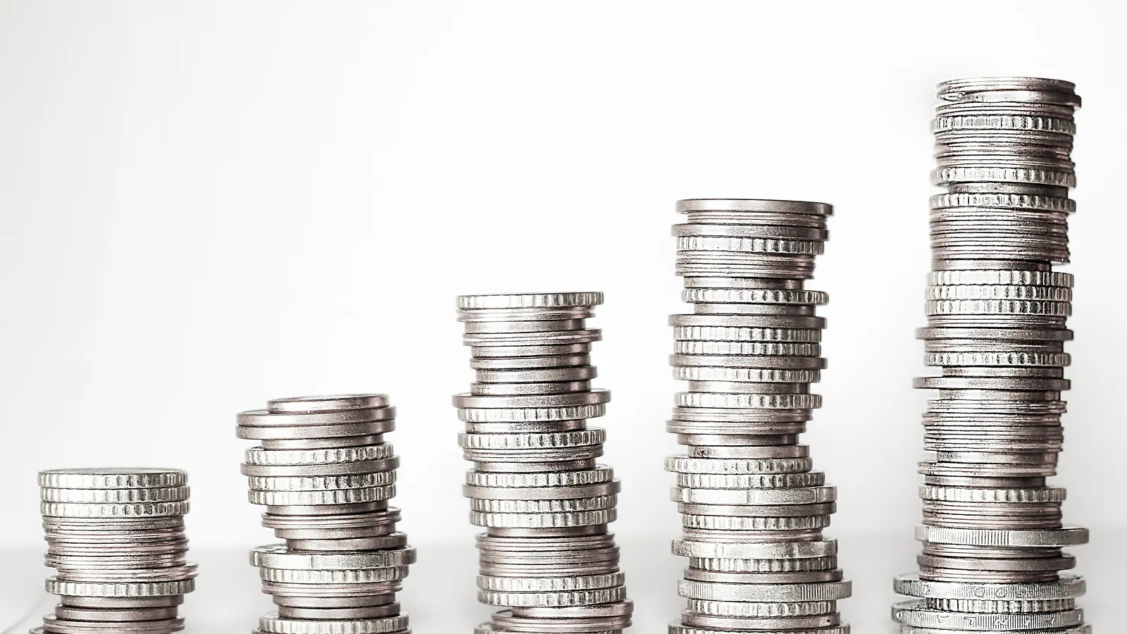 Several stacks of silver coins on a white surface, each stack taller than the one before.