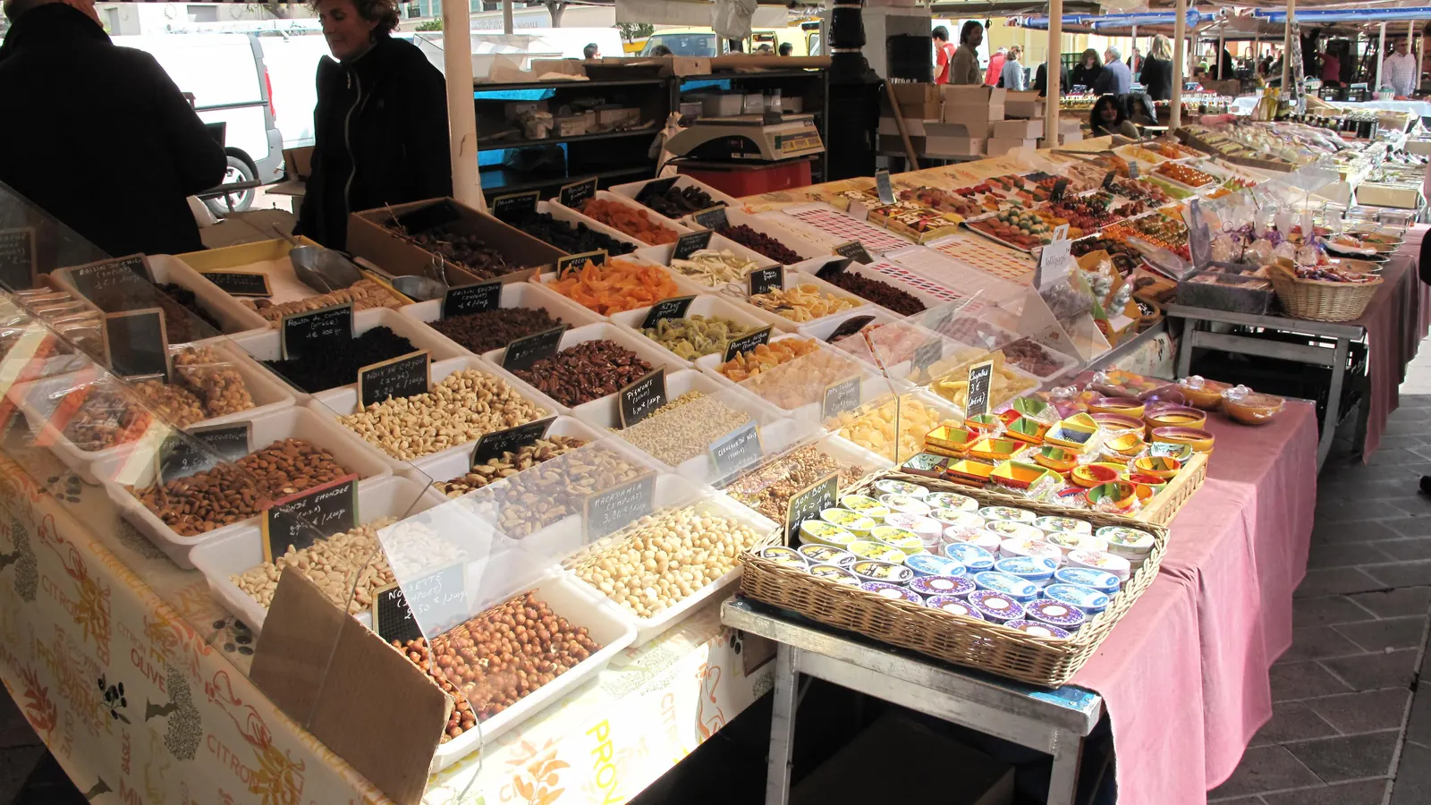A busy market stall with white bins of nuts, dried fruit and candied sweets on long tables