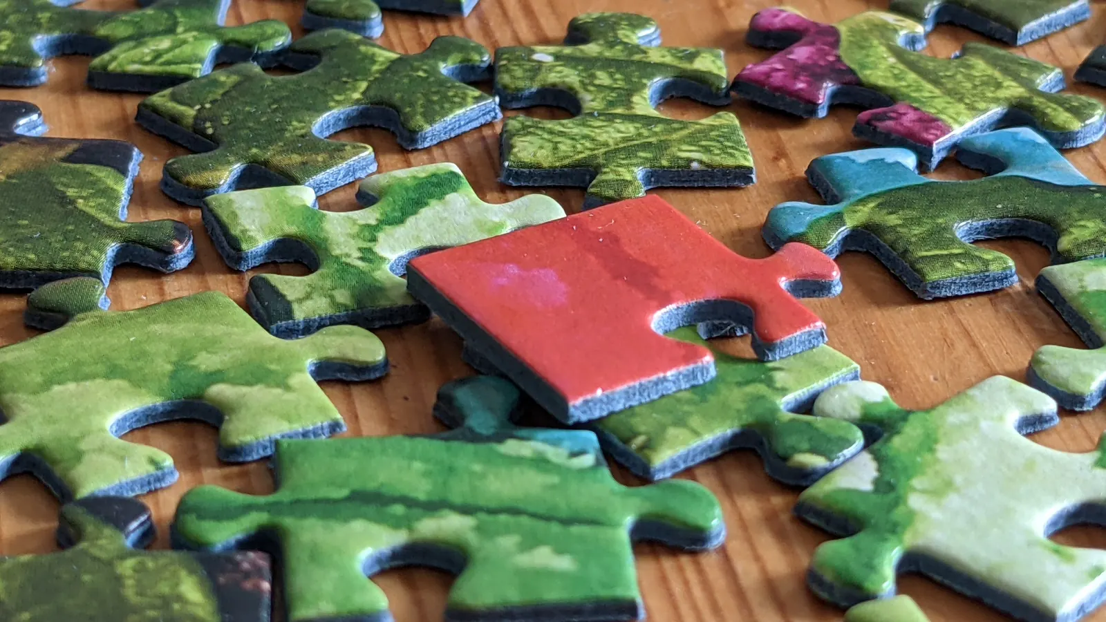 One red jigsaw piece stands out among green puzzle pieces on a flat surface