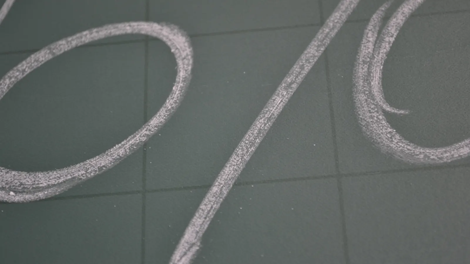 A percent sign drawn in chalk on a gray surface, seen from above.