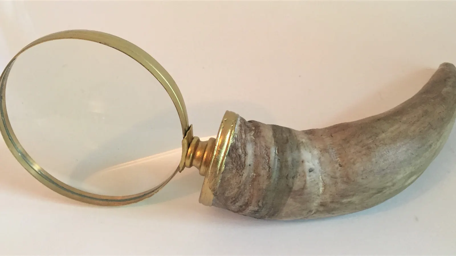 A brass-rimmed magnifying glass on a curved horn handle, shown on a plain white background.