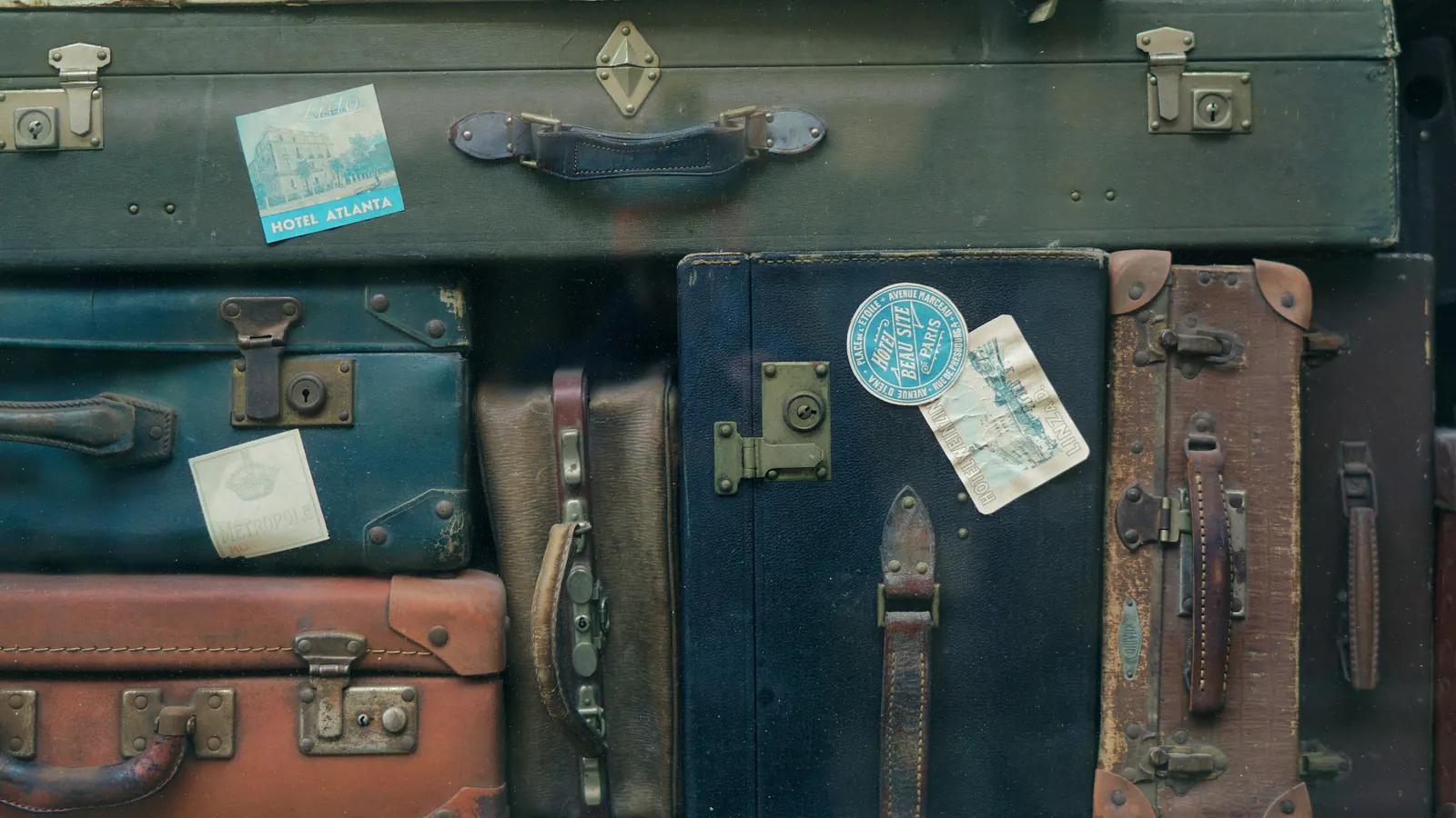 A tall stack of weathered vintage suitcases with leather handles, latches and travel stickers