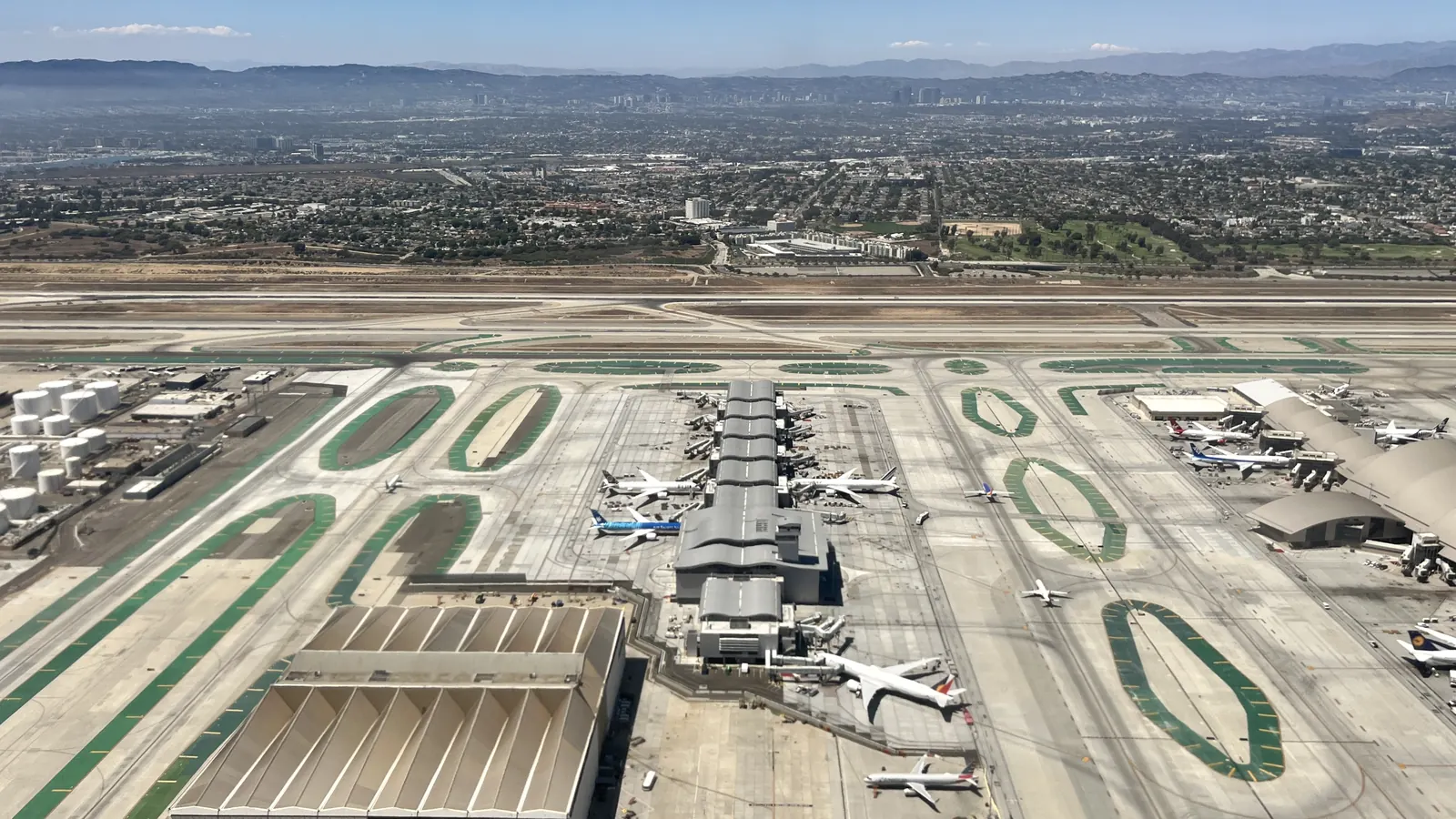 Aerial view of an airport with planes parked at terminal gates and runways beyond.