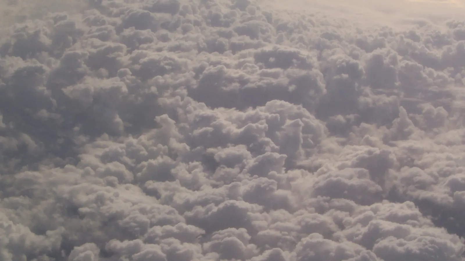Soft white clouds fill the frame, seen from high above the ground.
